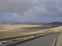 a road with an empty section below the mountain and clouds overhead above it in the distance,