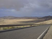 a road with an empty section below the mountain and clouds overhead above it in the distance,