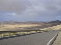 a road with an empty section below the mountain and clouds overhead above it in the distance,