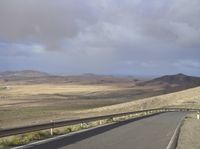 a road with an empty section below the mountain and clouds overhead above it in the distance,