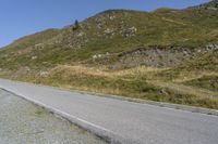 a curve road stretches into the distance on the hillside top next to a grassy hillside