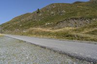 a curve road stretches into the distance on the hillside top next to a grassy hillside