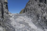 a large cliff face with a person standing on top of it and a mountaintop near the side of it