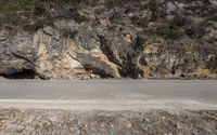 a motorcycle is parked on the side of the road near a cliff with a cave in the background