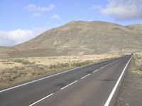 a long paved highway that winds along a mountainous valley in the distance is a hill