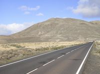 a long paved highway that winds along a mountainous valley in the distance is a hill