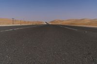 a highway is pictured through the desert and looks straight ahead with sand mountains in the background