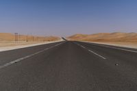 a highway is pictured through the desert and looks straight ahead with sand mountains in the background