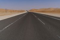 a highway is pictured through the desert and looks straight ahead with sand mountains in the background