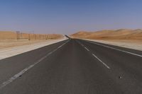 a highway is pictured through the desert and looks straight ahead with sand mountains in the background