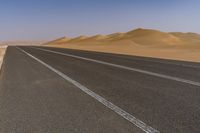 a lone motorcycle is driving on a desert highway near dunes and sand dunes on the horizon