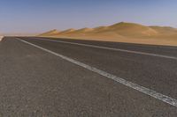 a lone motorcycle is driving on a desert highway near dunes and sand dunes on the horizon