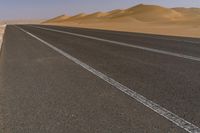 a lone motorcycle is driving on a desert highway near dunes and sand dunes on the horizon