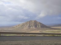 a large mountain behind the highway near a roadway with a fence on the side of the road