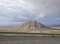 a large mountain behind the highway near a roadway with a fence on the side of the road