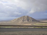 a large mountain behind the highway near a roadway with a fence on the side of the road