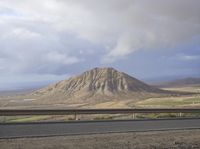 a large mountain behind the highway near a roadway with a fence on the side of the road