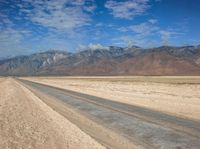 an empty desert road on a sunny day in the desert, with snowcapped mountains behind