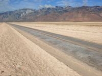 an empty desert road on a sunny day in the desert, with snowcapped mountains behind