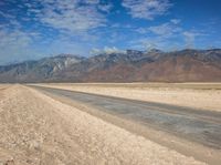 an empty desert road on a sunny day in the desert, with snowcapped mountains behind