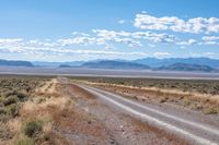 a single road leads through the open plain to mountains and clouds above them from a distance