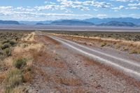 a single road leads through the open plain to mountains and clouds above them from a distance