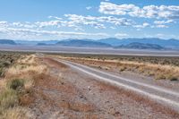 a single road leads through the open plain to mountains and clouds above them from a distance