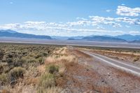 a single road leads through the open plain to mountains and clouds above them from a distance