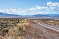 a single road leads through the open plain to mountains and clouds above them from a distance