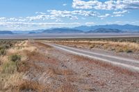 a single road leads through the open plain to mountains and clouds above them from a distance