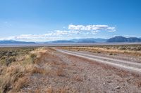 a single road leads through the open plain to mountains and clouds above them from a distance