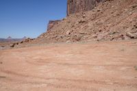 a dirt road through a desert plain with a mountain behind it and a clear blue sky in the background