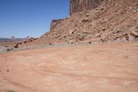 a dirt road through a desert plain with a mountain behind it and a clear blue sky in the background