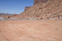 a dirt road through a desert plain with a mountain behind it and a clear blue sky in the background