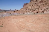 a dirt road through a desert plain with a mountain behind it and a clear blue sky in the background