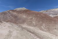 several hills have various colors on them in the desert with blue skies above them and a few dark shadows on them