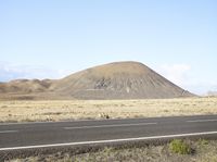 a mountain with a road next to it and some grass and dirt with trees on the side of it