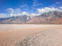 a very barren desert with mountains in the background and clouds in the distance at this time of the day