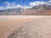 a very barren desert with mountains in the background and clouds in the distance at this time of the day