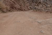 a person riding a bike down a dirt road in the mountains around it and a rock cliff