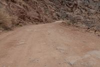 a person riding a bike down a dirt road in the mountains around it and a rock cliff