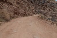 a person riding a bike down a dirt road in the mountains around it and a rock cliff