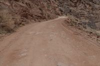 a person riding a bike down a dirt road in the mountains around it and a rock cliff