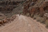 a person riding a bike down a dirt road in the mountains around it and a rock cliff