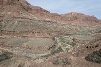 a lone rider rides through the landscape and overlooks a gorge below them in an arid area