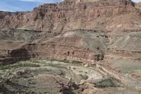 a lone rider rides through the landscape and overlooks a gorge below them in an arid area