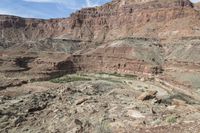 a lone rider rides through the landscape and overlooks a gorge below them in an arid area