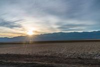 an open plain with the sun peeking over the mountains in the distance and the sun setting on the horizon