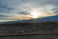 an open plain with the sun peeking over the mountains in the distance and the sun setting on the horizon