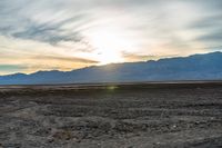 an open plain with the sun peeking over the mountains in the distance and the sun setting on the horizon